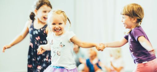 Three girls are holding hands and dancing in a semicircle.