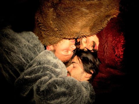 Three people, wrapped in fluffy blankets, snuggle up together so they can sleep more comfortably in the cold.