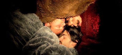 Three people, wrapped in fluffy blankets, snuggle up together so they can sleep more comfortably in the cold.
