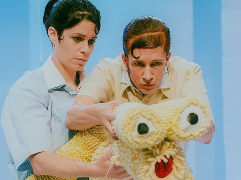 Two actresses, with artfully styled, immaculate hairstyles, are intently holding a cuddly creature with two large eyes and a red mouth.